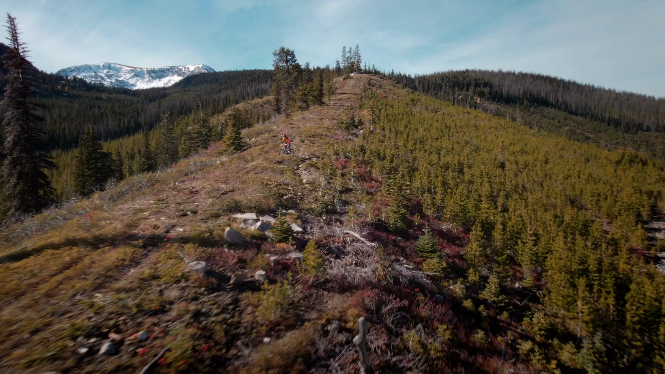 Aerial along a ridge trail with snowy peaks ahead