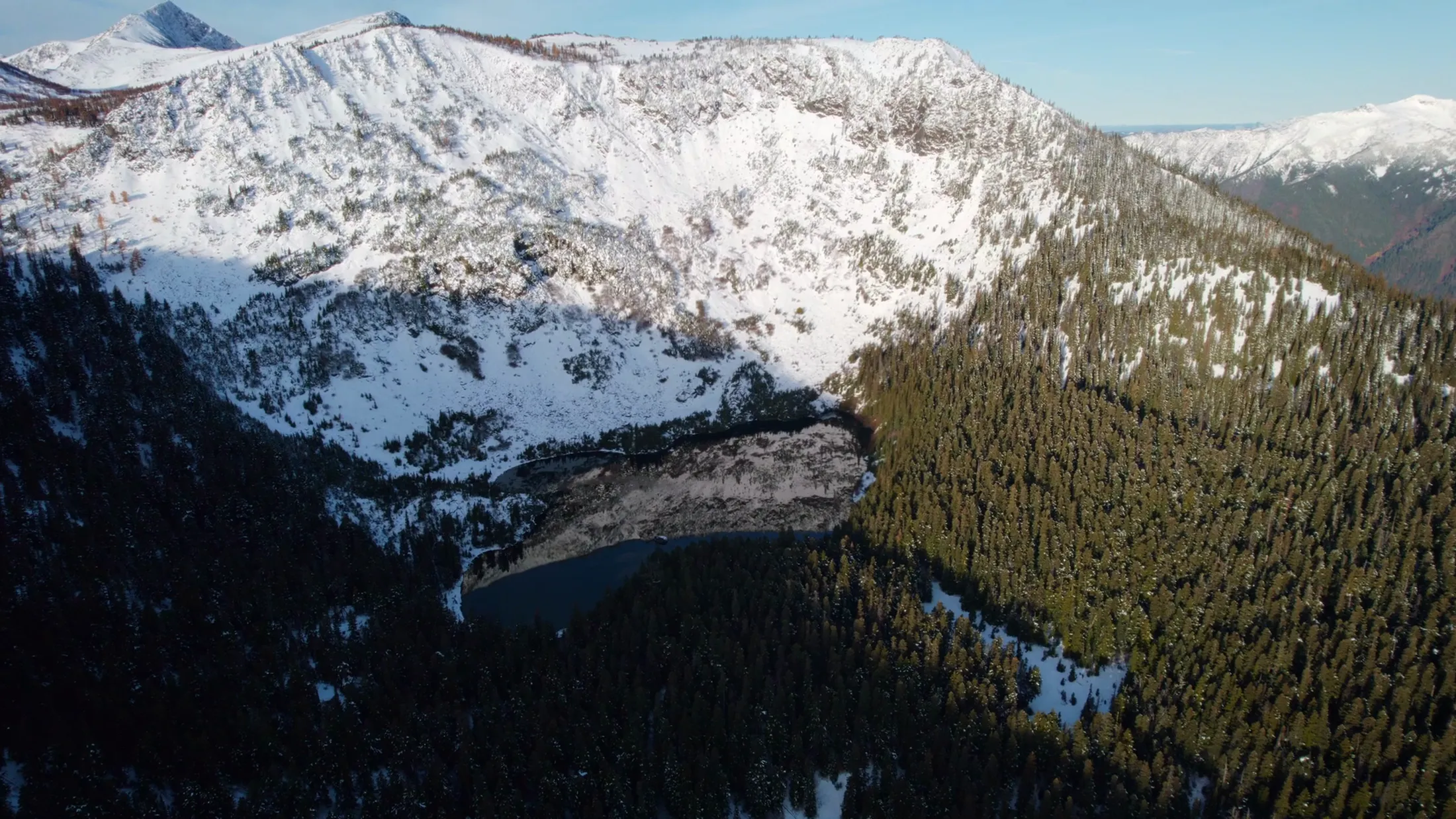 Aerial of a snowy cirque above dark forest