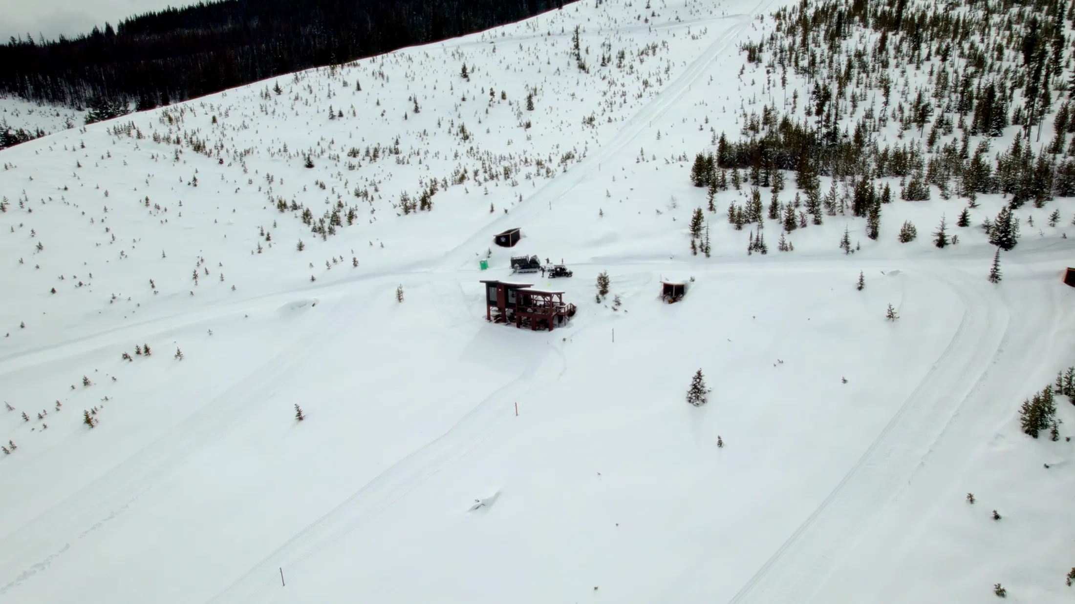 Aerial of a cabin and snowcat on a white slope