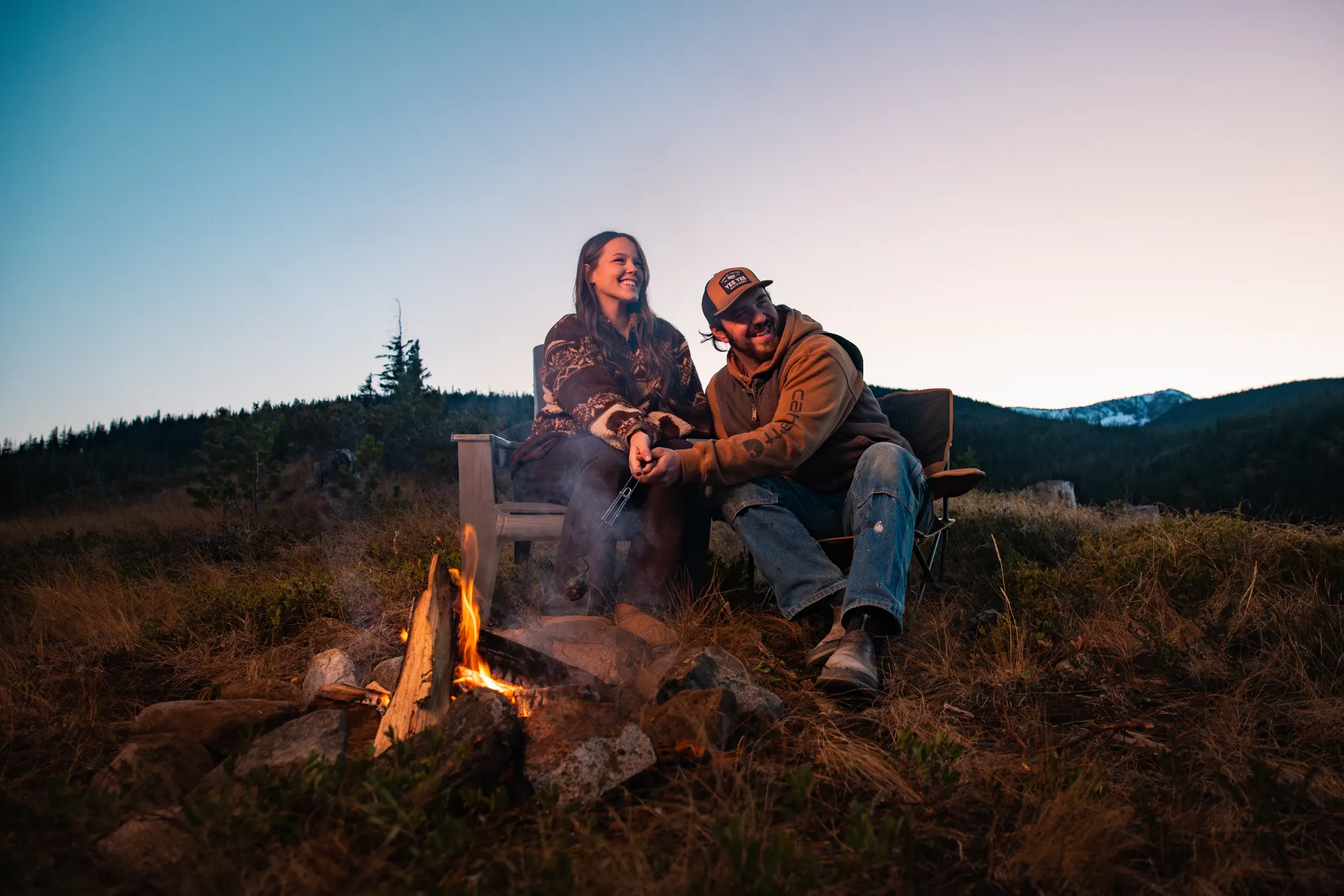 Two people by a campfire at dusk on the mountain