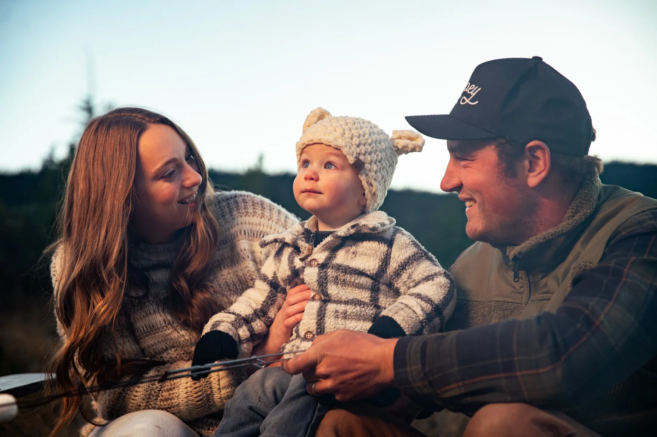 A couple and their baby laughing by the fire