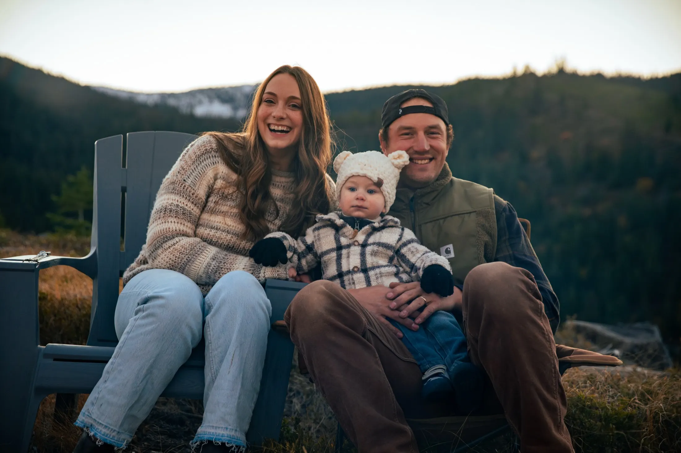 Family smiling in camp chairs by the fire