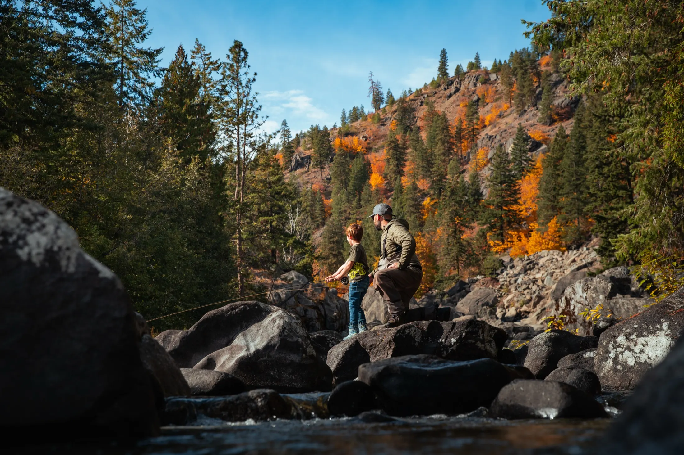Father and son fishing from boulders under fall color