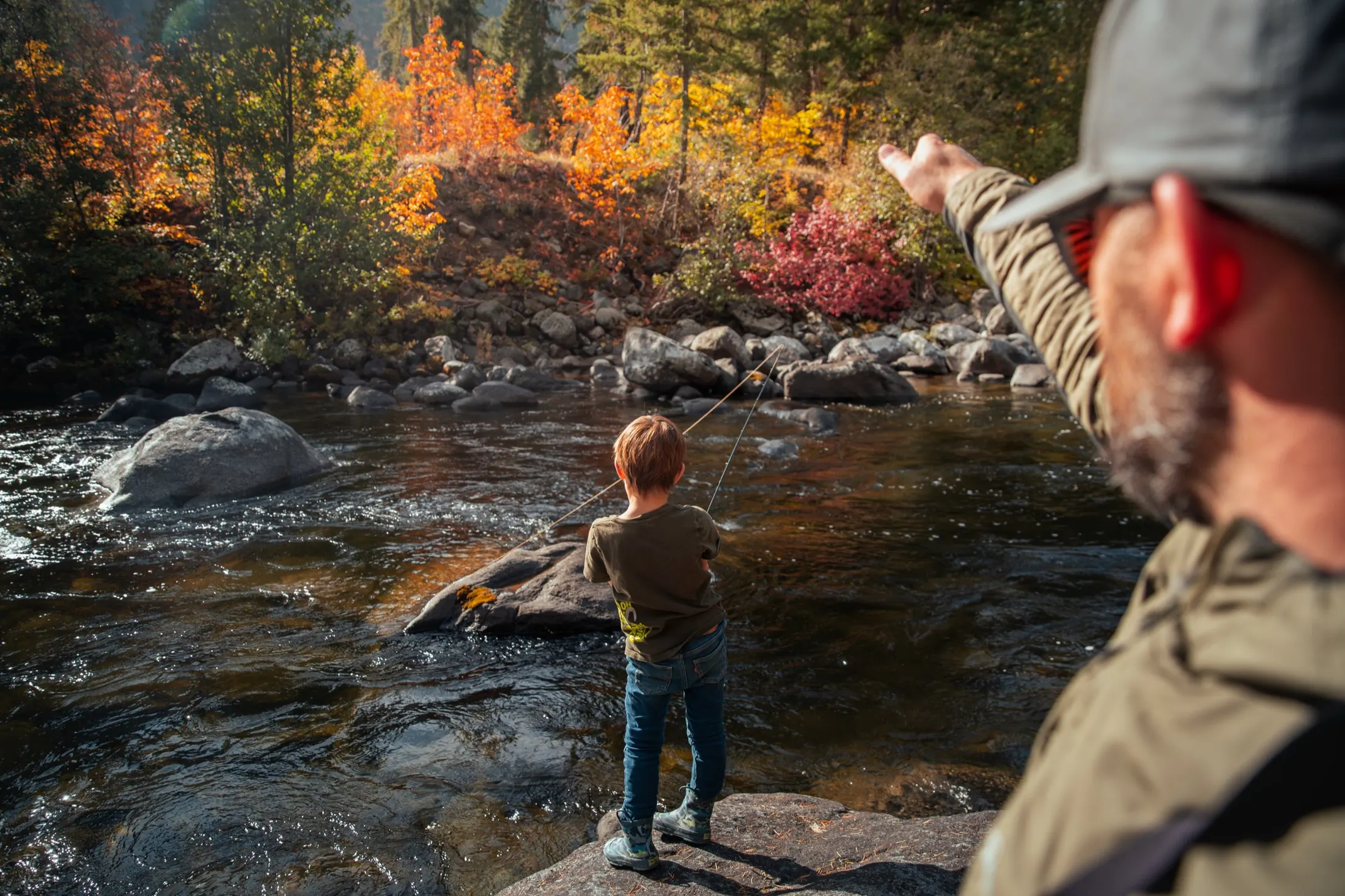 Boy fishing a stream while his dad points the way