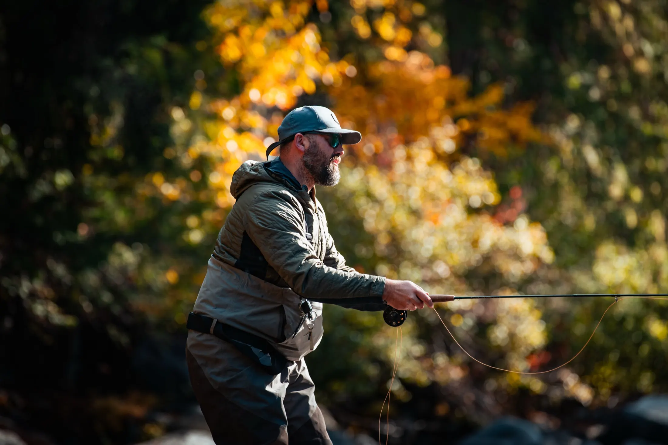 Angler casting with fall color behind him