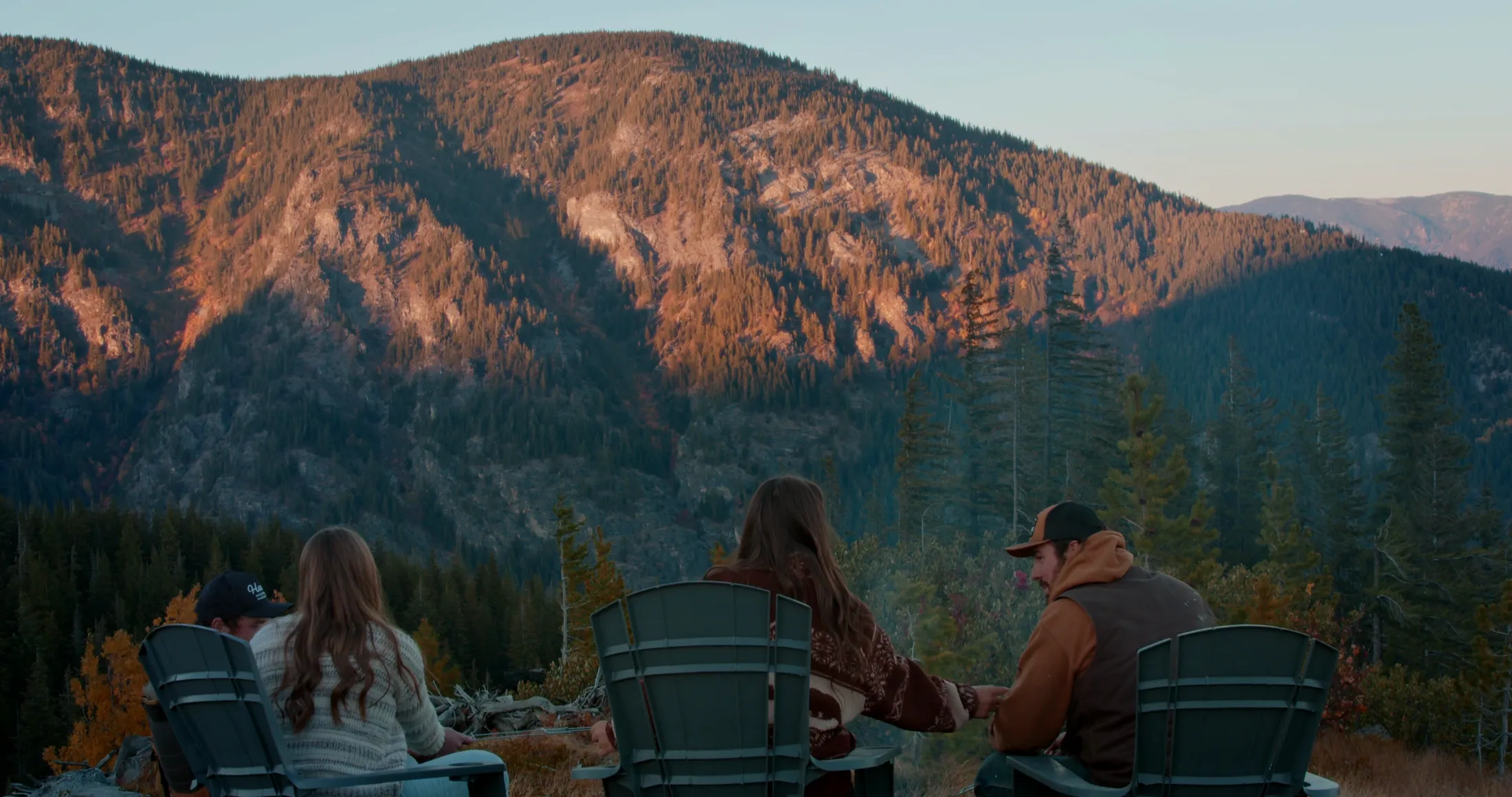 Friends in chairs facing an alpenglow-lit mountain