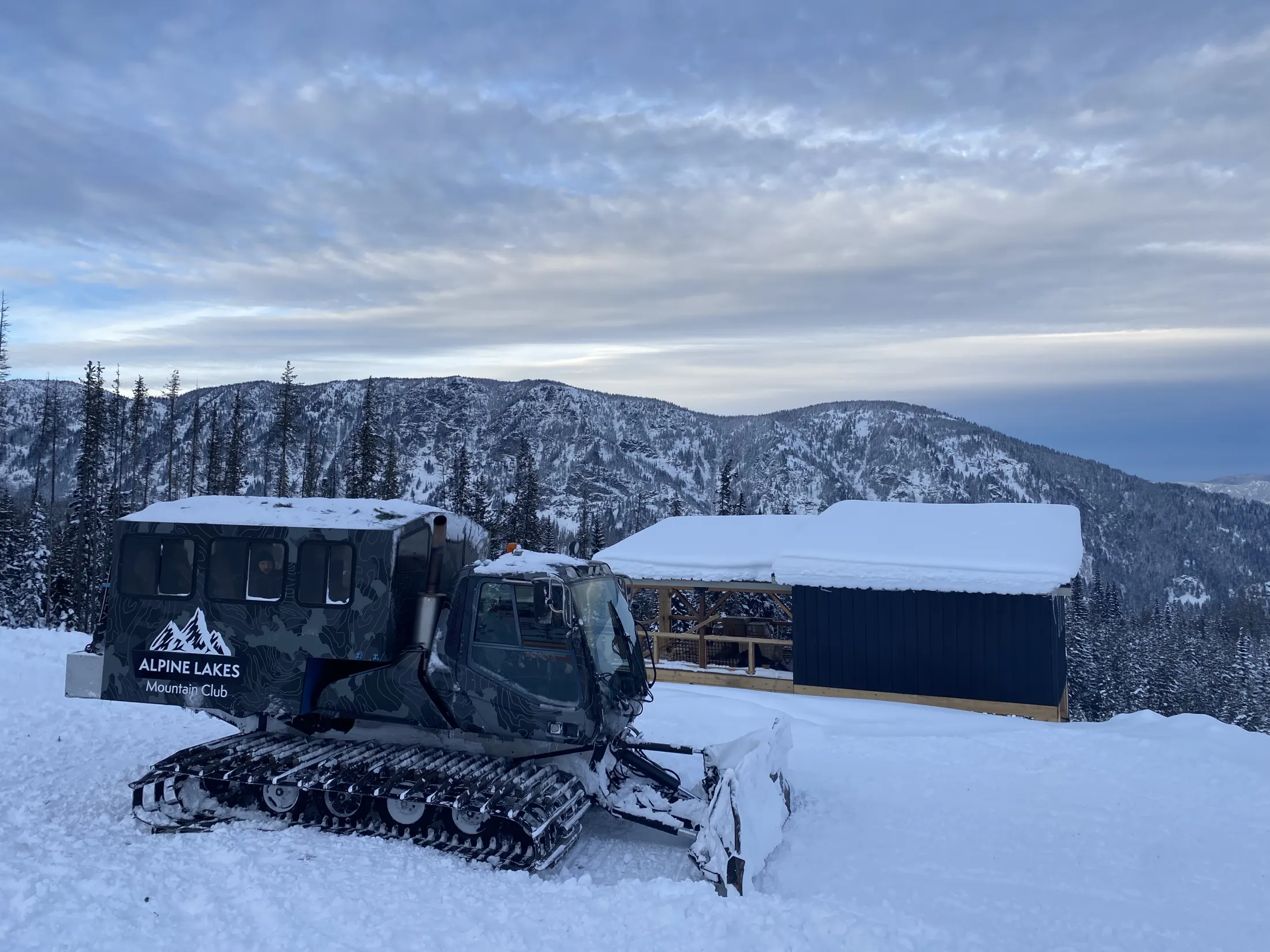 Snowcat parked beside a cabin under a winter sky