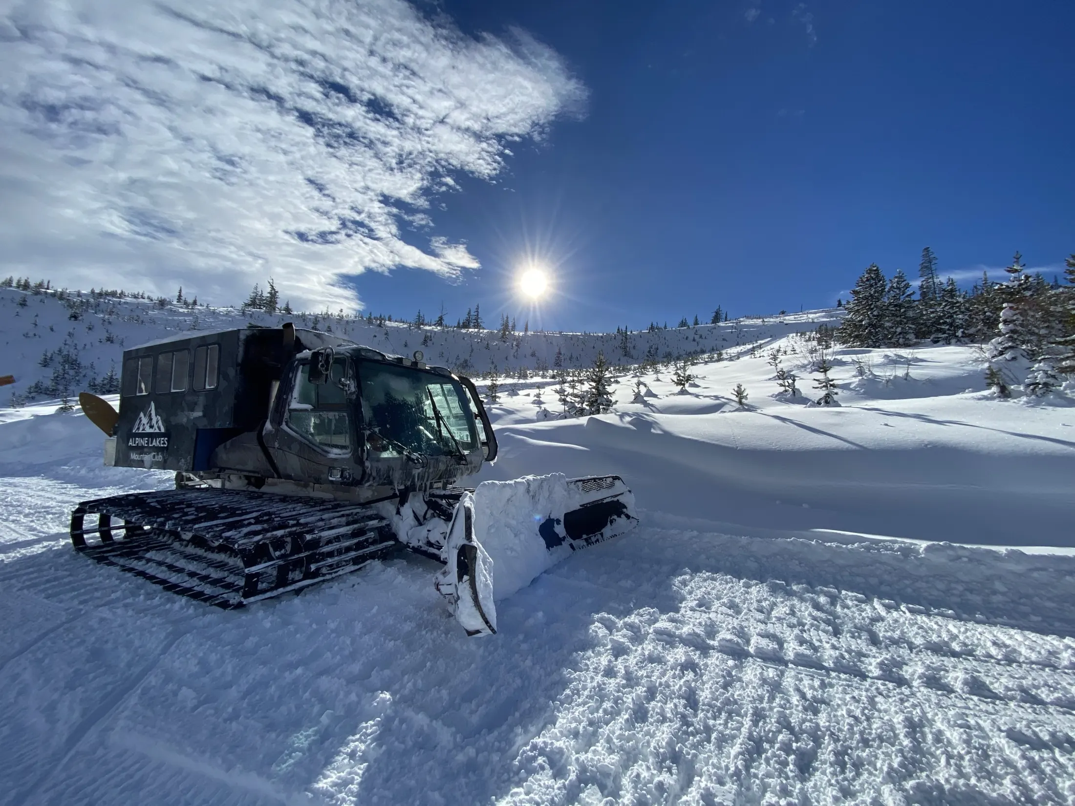 Snowcat on a groomed track with the sun overhead