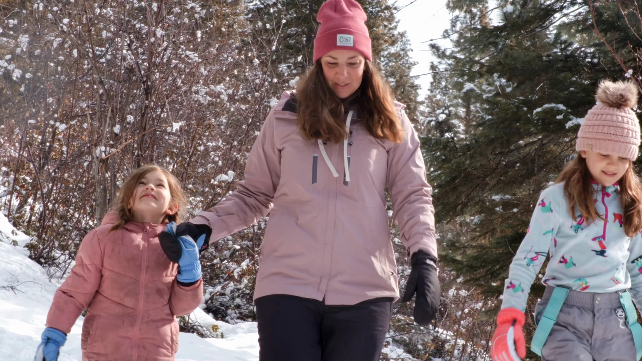 A mother and two daughters walking through snowy woods