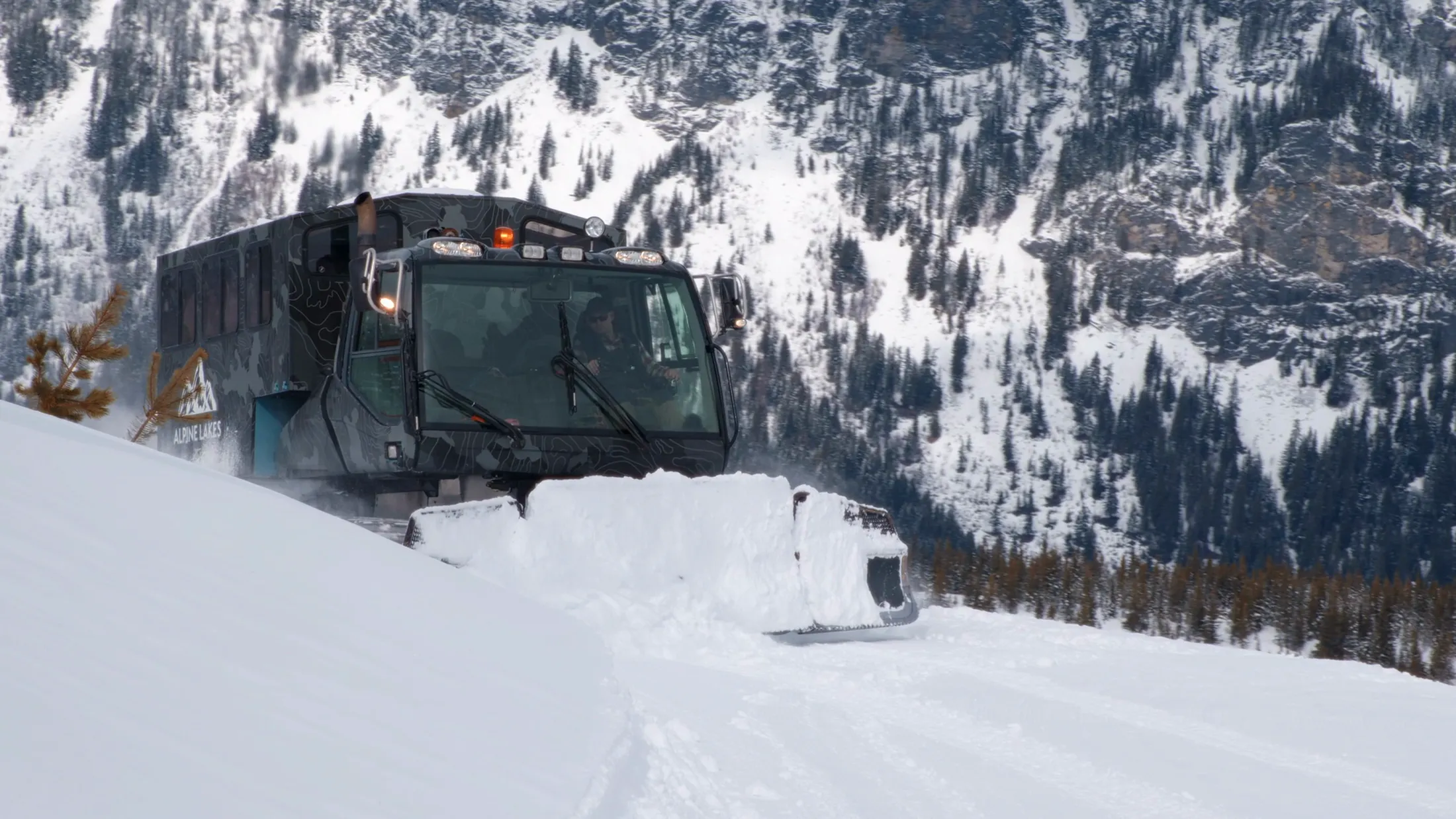 Snowcat climbing a ridge below snowy cliffs