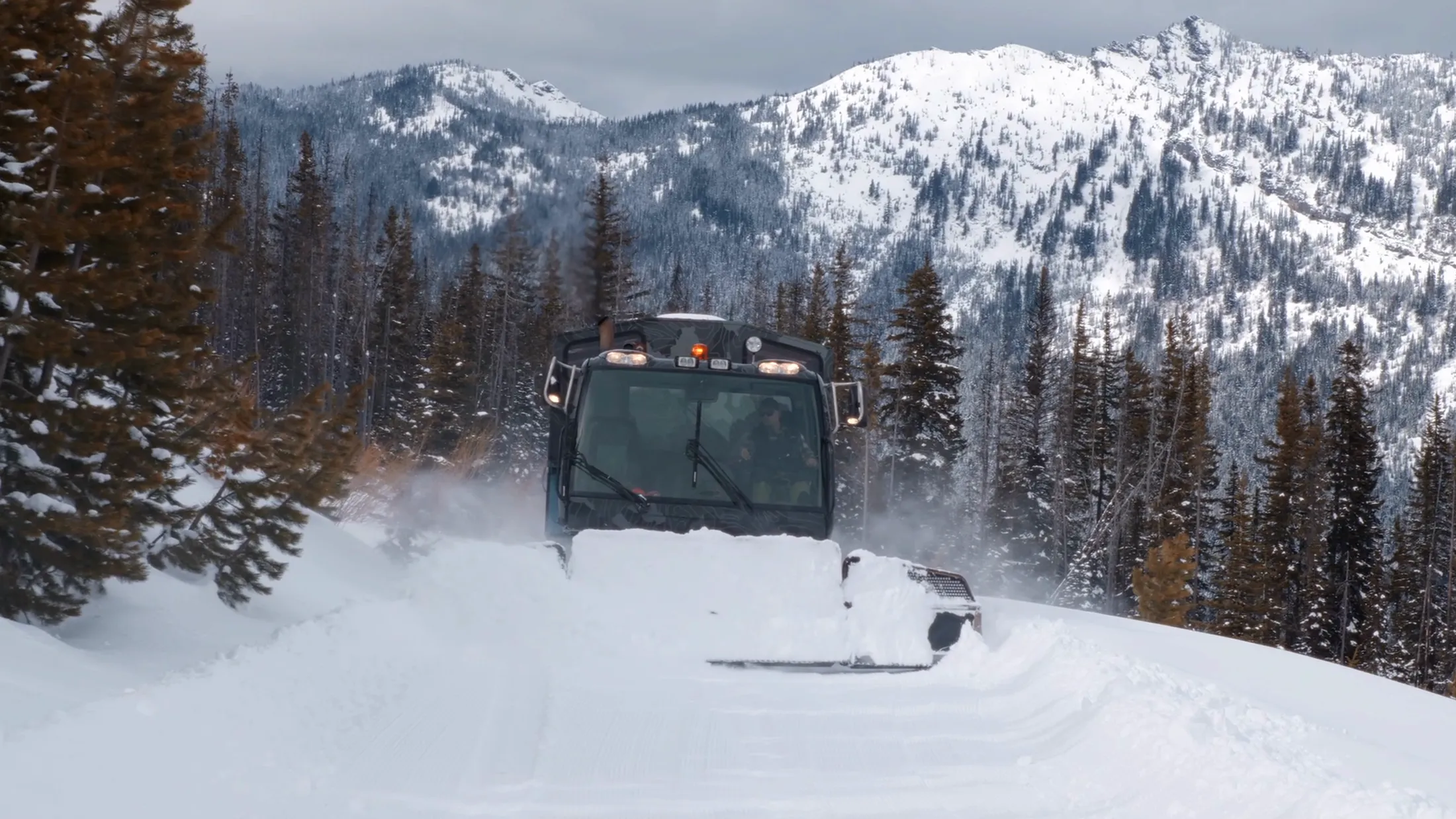 Snowcat crossing below jagged snowy peaks